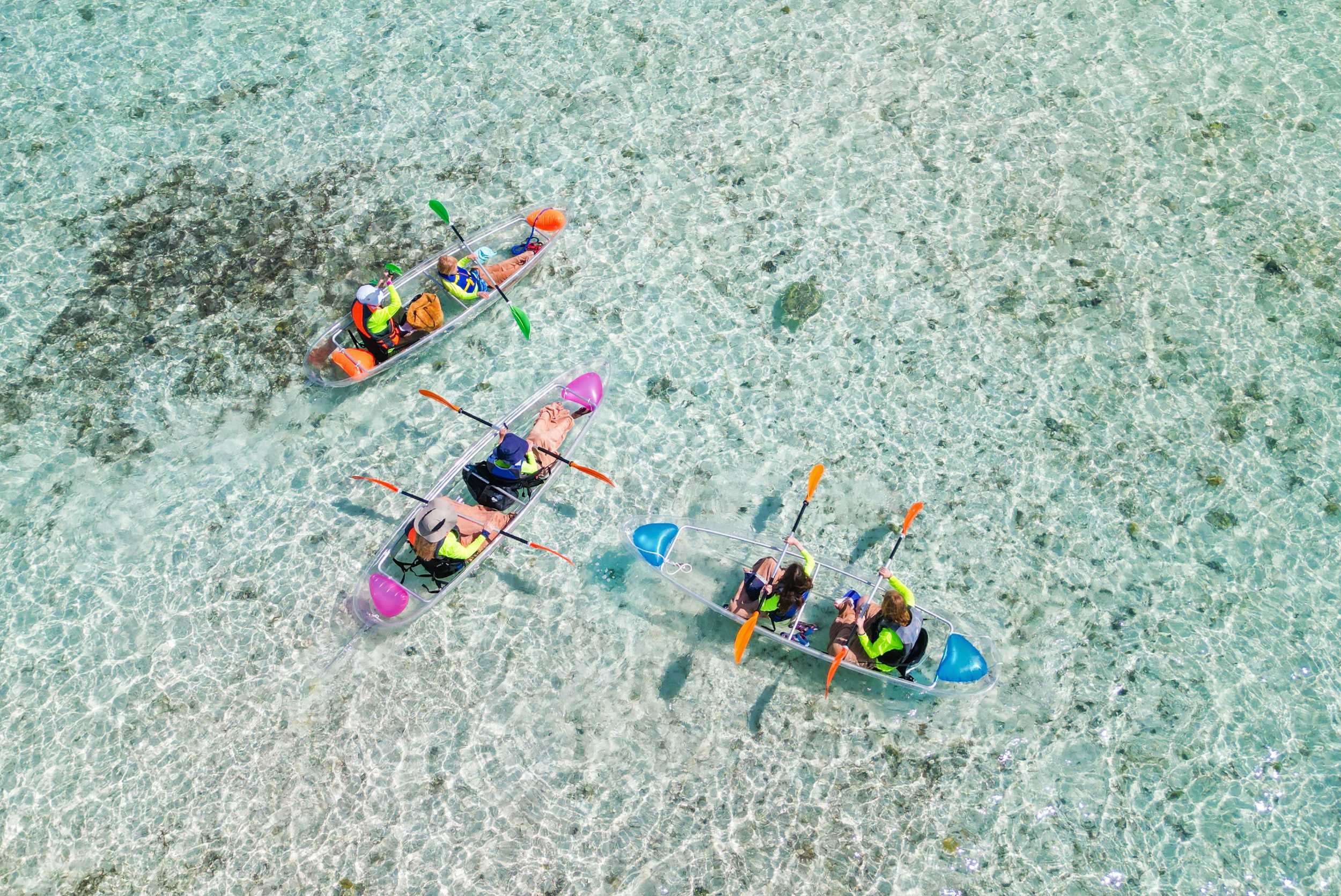 Overhead view of people kayaking in clear shallow water with rocks visible beneath.