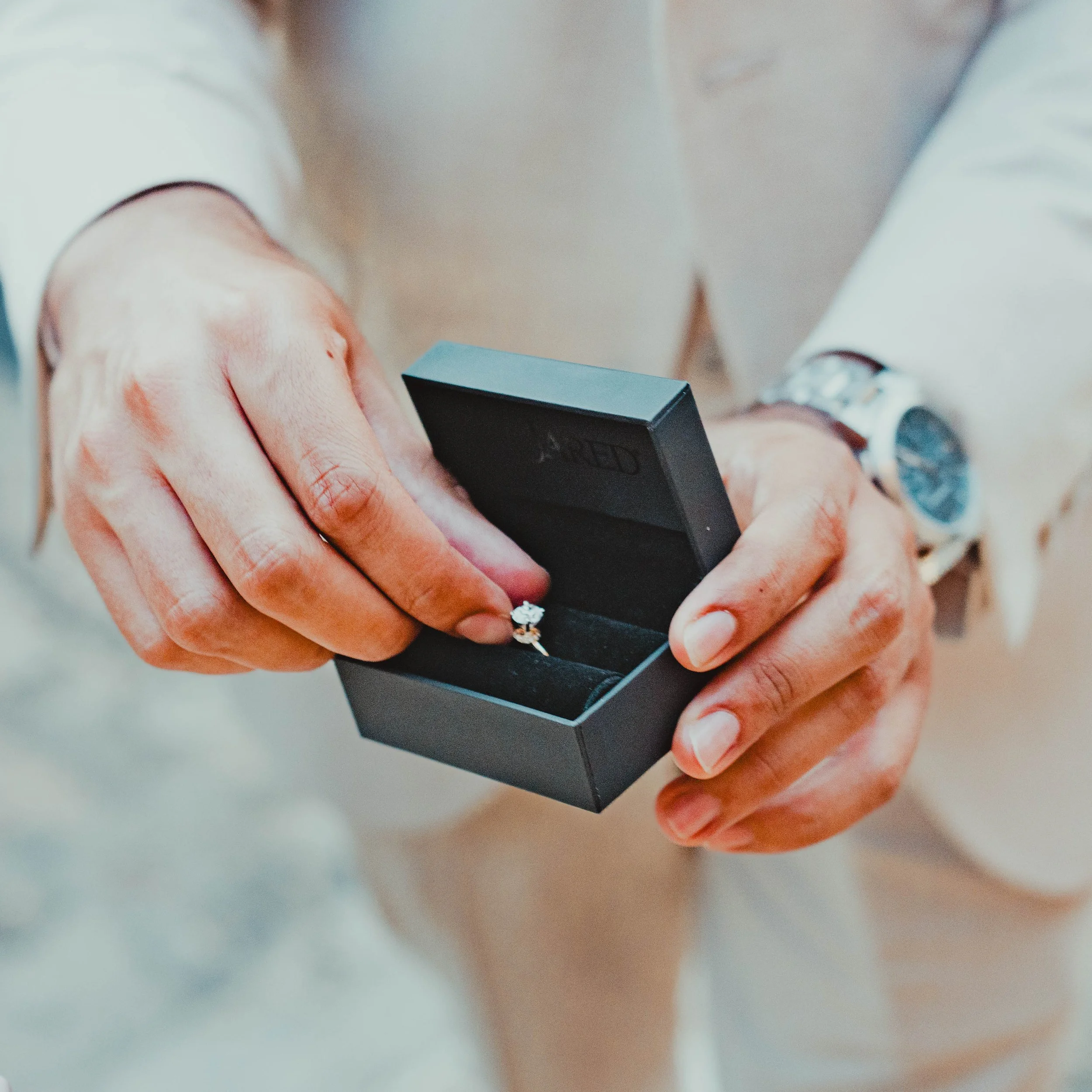 Close-up of a person's hand holding a black box, focusing on the fingers and the box, with a blurred background.