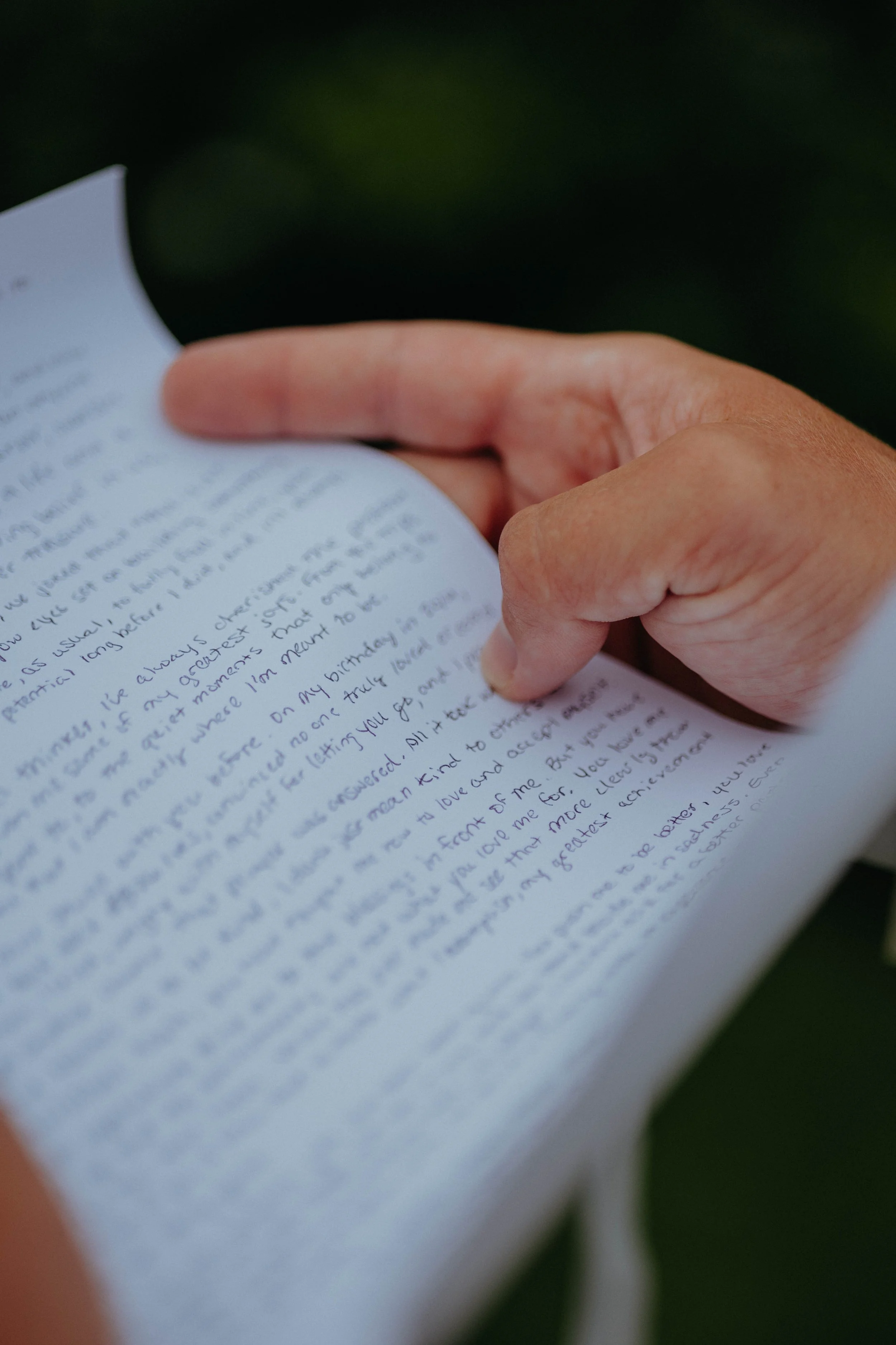 Close-up of a person's hand holding and turning a handwritten letter or note on a piece of paper.