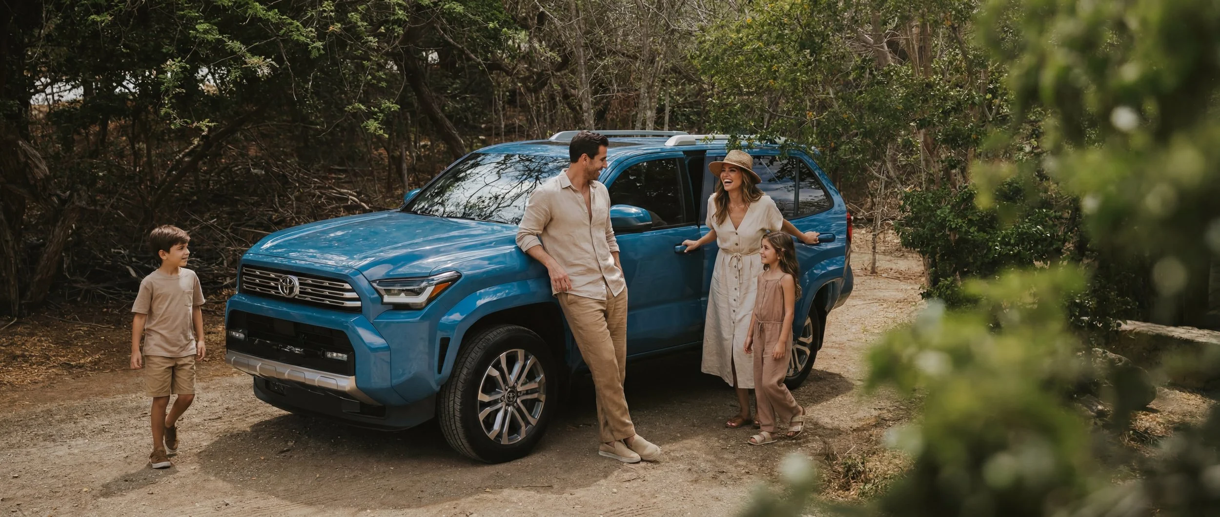Family of four enjoying a walk near a blue Toyota SUV in a wooded area, with trees and foliage surrounding them.