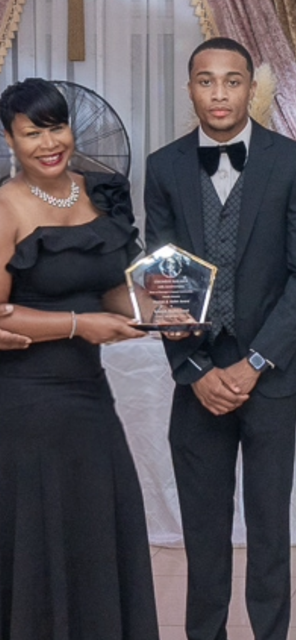 Brisa Builders Corp. A woman in a black dress holding an award, standing next to a man in a tuxedo at a formal event.