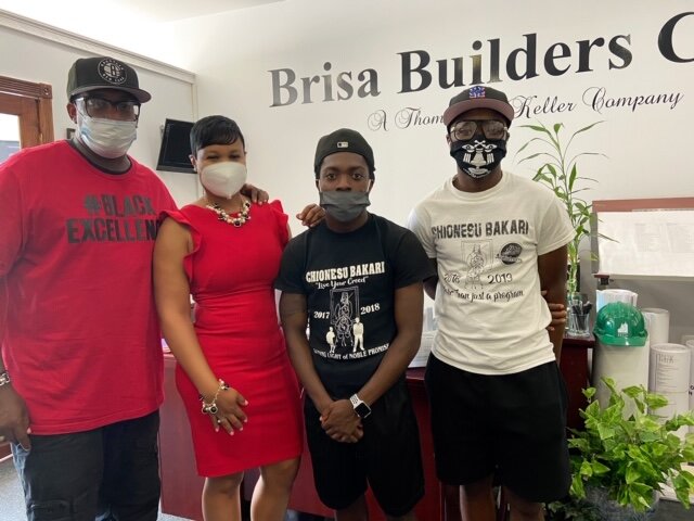 Brisa Builders Corp. Four people standing in front of a sign that reads "Brisa Builders." They are all wearing face masks and casual attire.