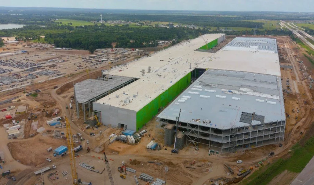 Aerial view of an under-construction large commercial building with some sections complete and others in progress, surrounded by construction equipment and dirt roads.