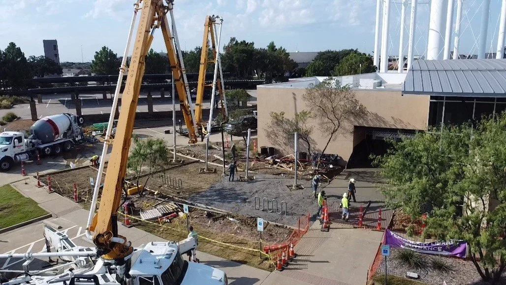 Construction workers and foundation equipment at a construction site outside a building with a concrete mixer truck nearby.