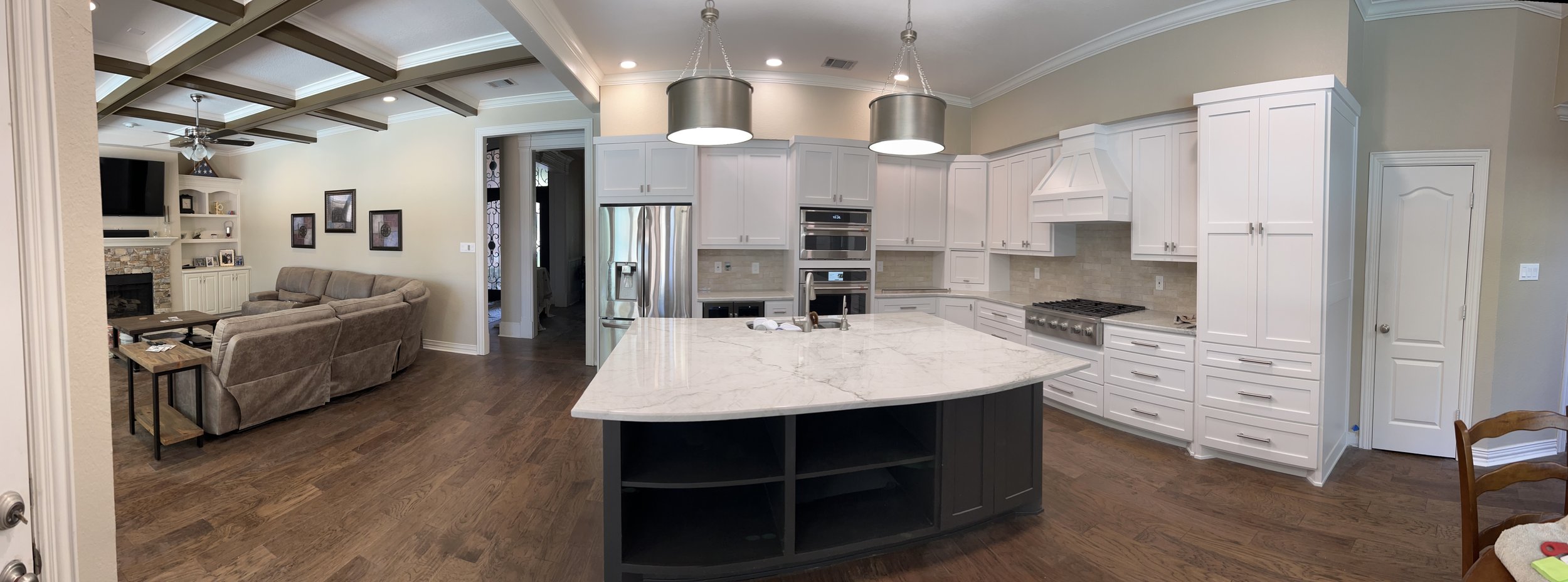Open-concept kitchen and living room with white cabinets, stainless steel appliances, marble island, and hardwood floors.