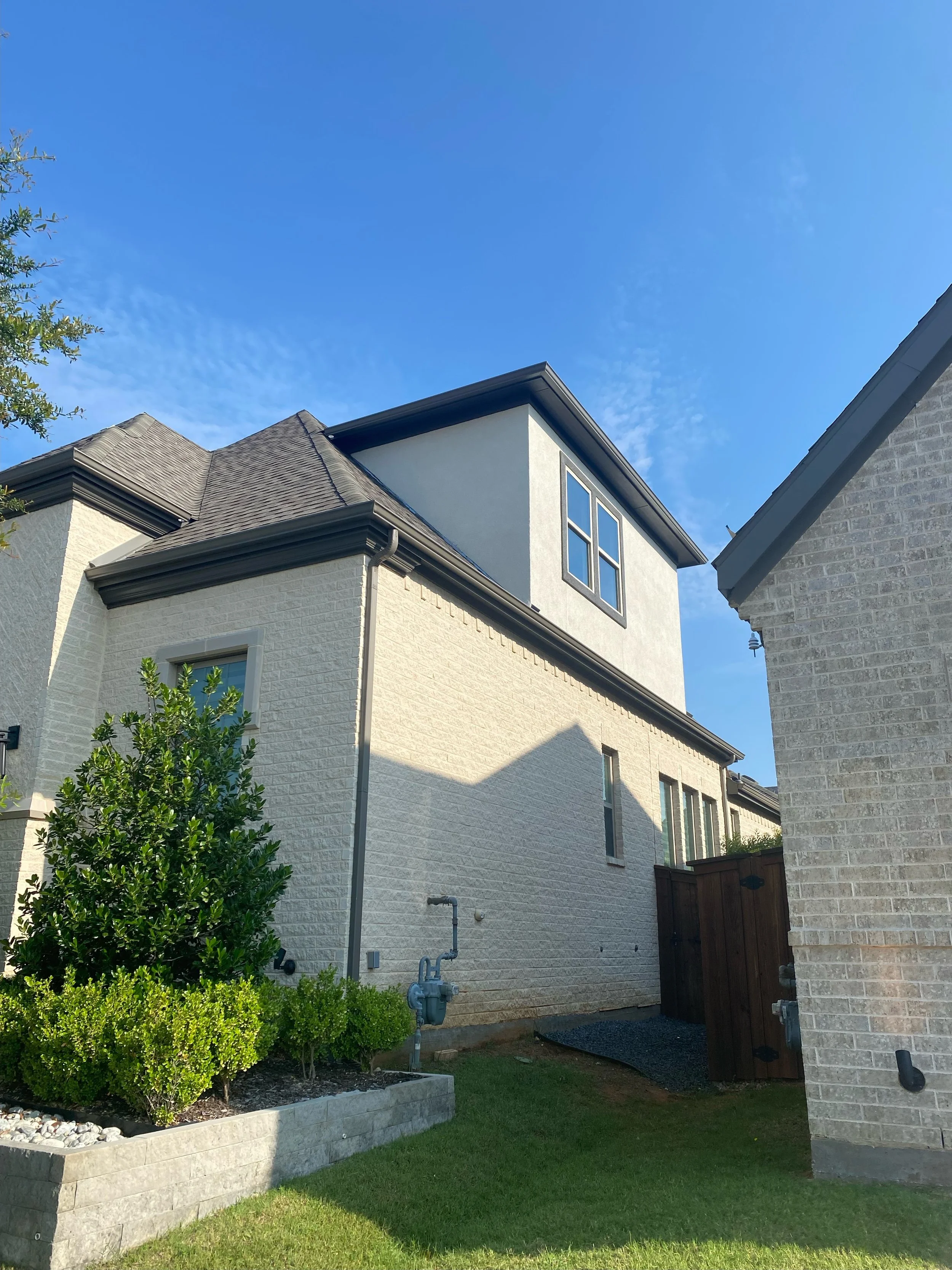 Backyard view of a home addition with brick wall, outdoor plants, green lawn