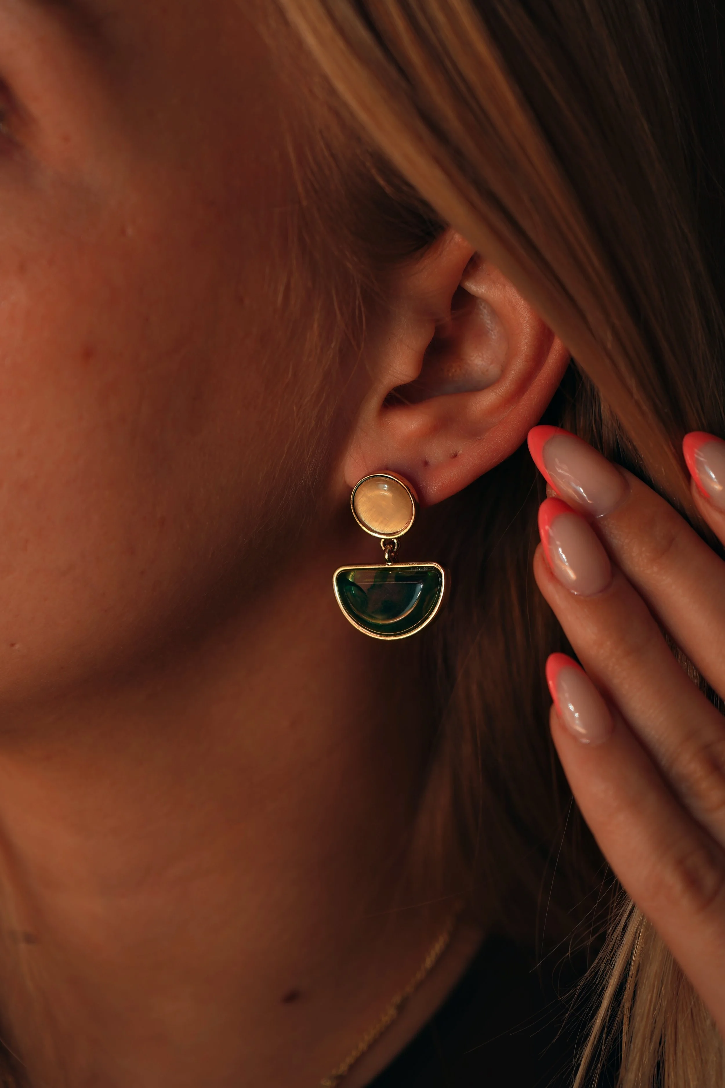 Nærbillede af en kvindes øre med en ørering og en finger med neglelak, der berører håret.