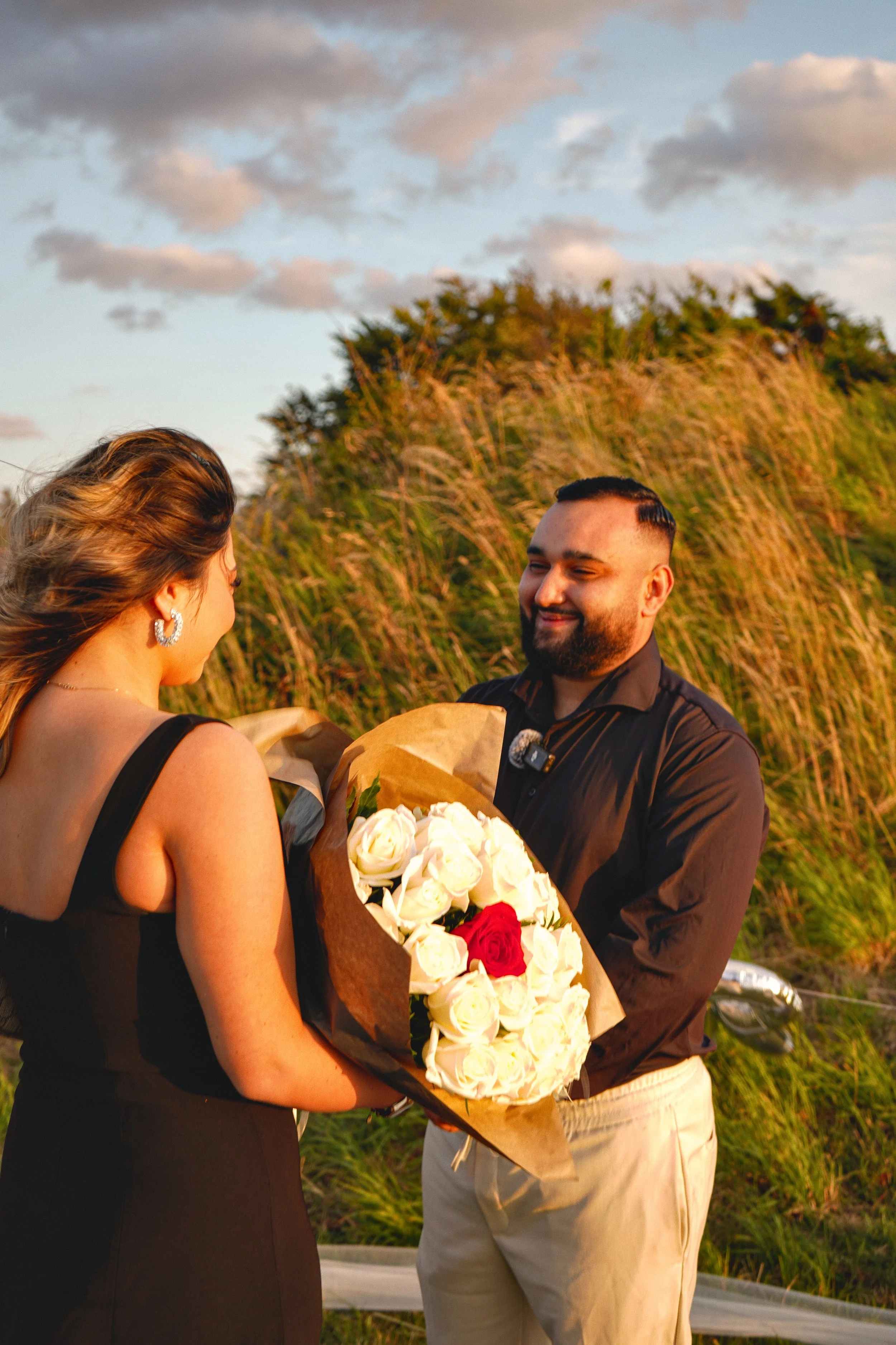 A man giving a woman a bouquet of white and red roses outdoors during sunset.