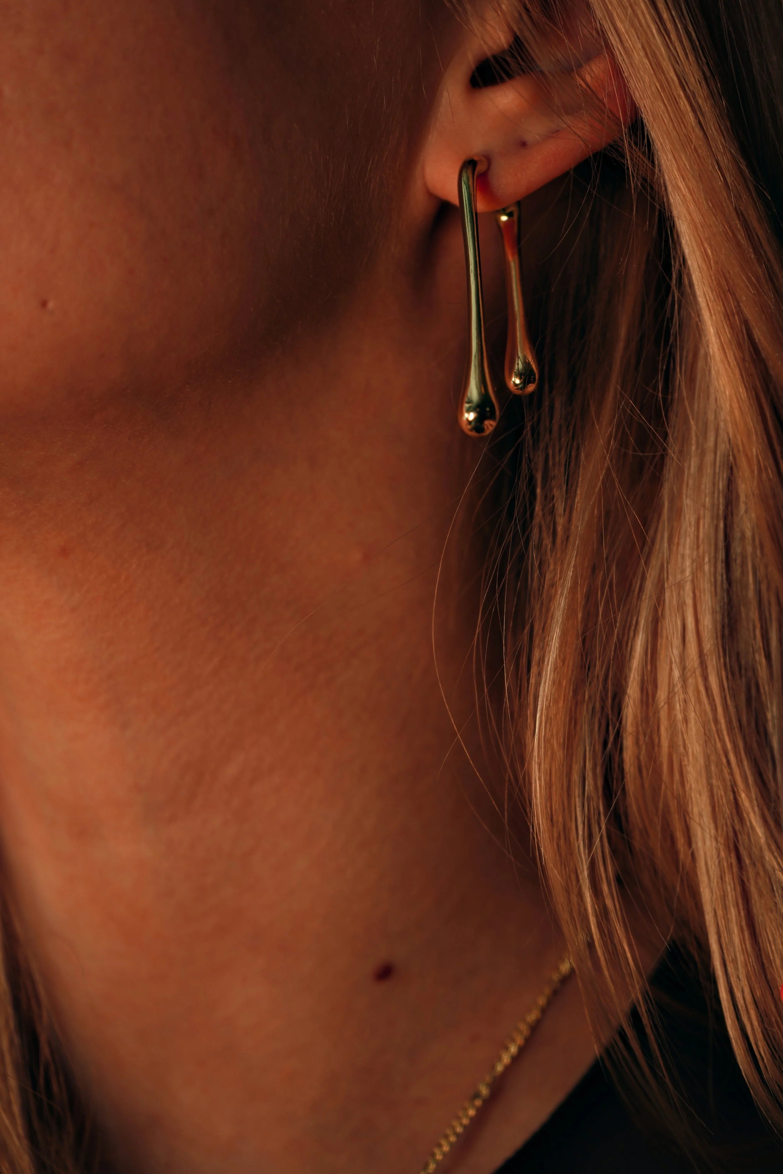 Nærbillede af en person med en guld ørering og halskæde, andengangs fokus på øret og halsen