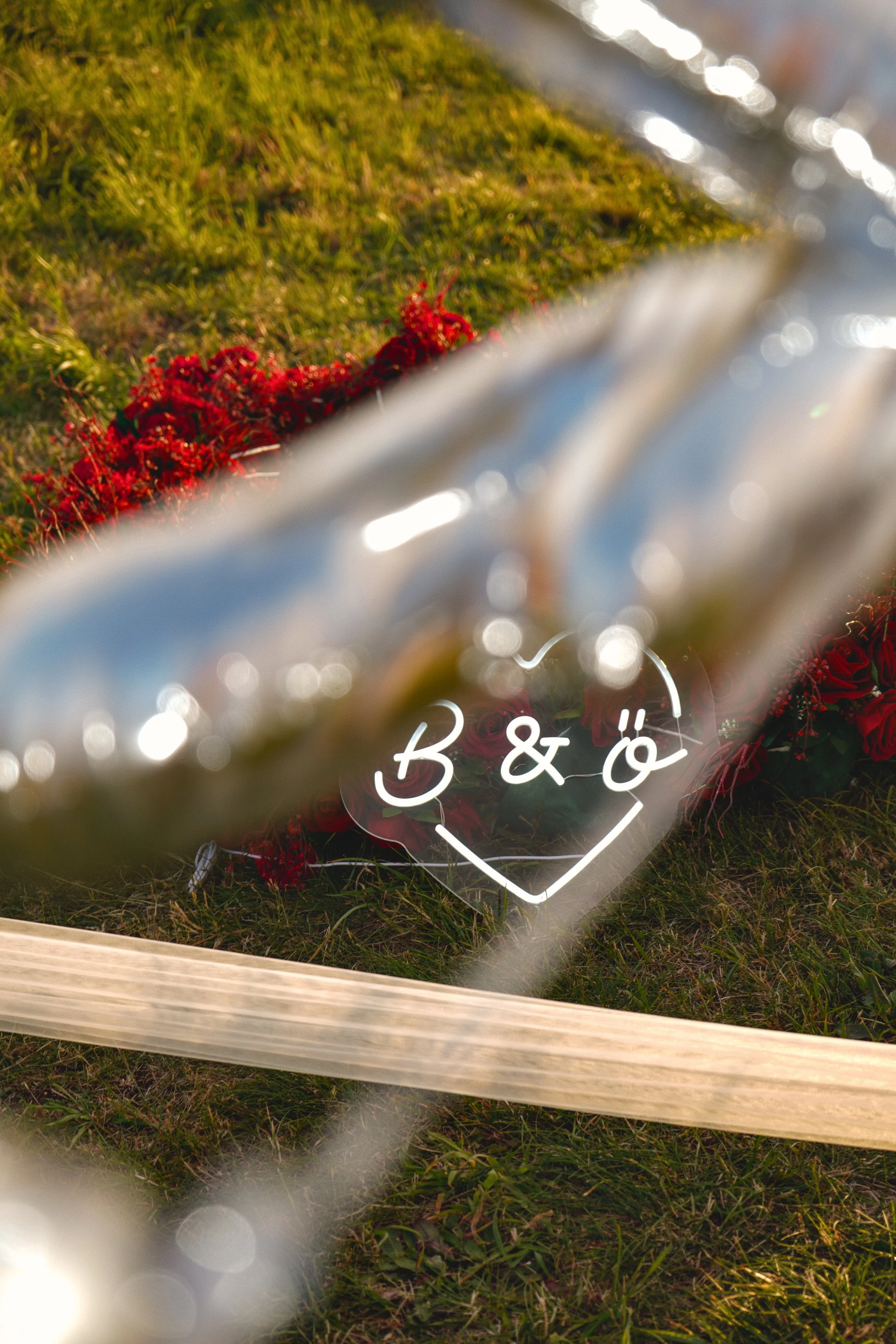 A memorial site with a wreath of red flowers on the ground, behind a chain-link fence with a bicycle lock attached, and a sign with the words 'B & Ö' inside a heart drawing.