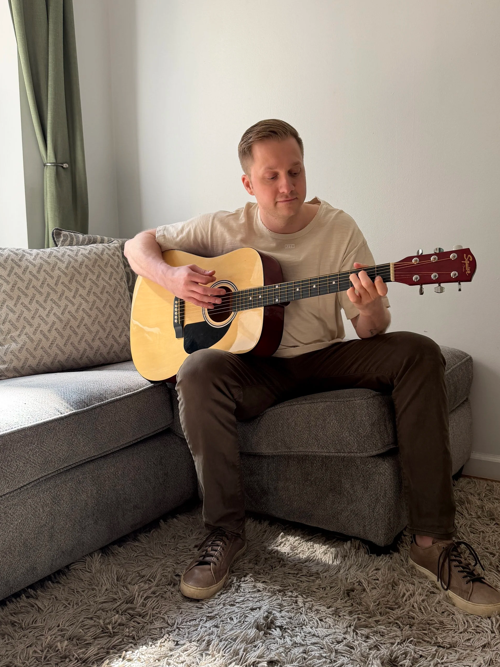 Jack Szary playing acoustic guitar on a couch at home