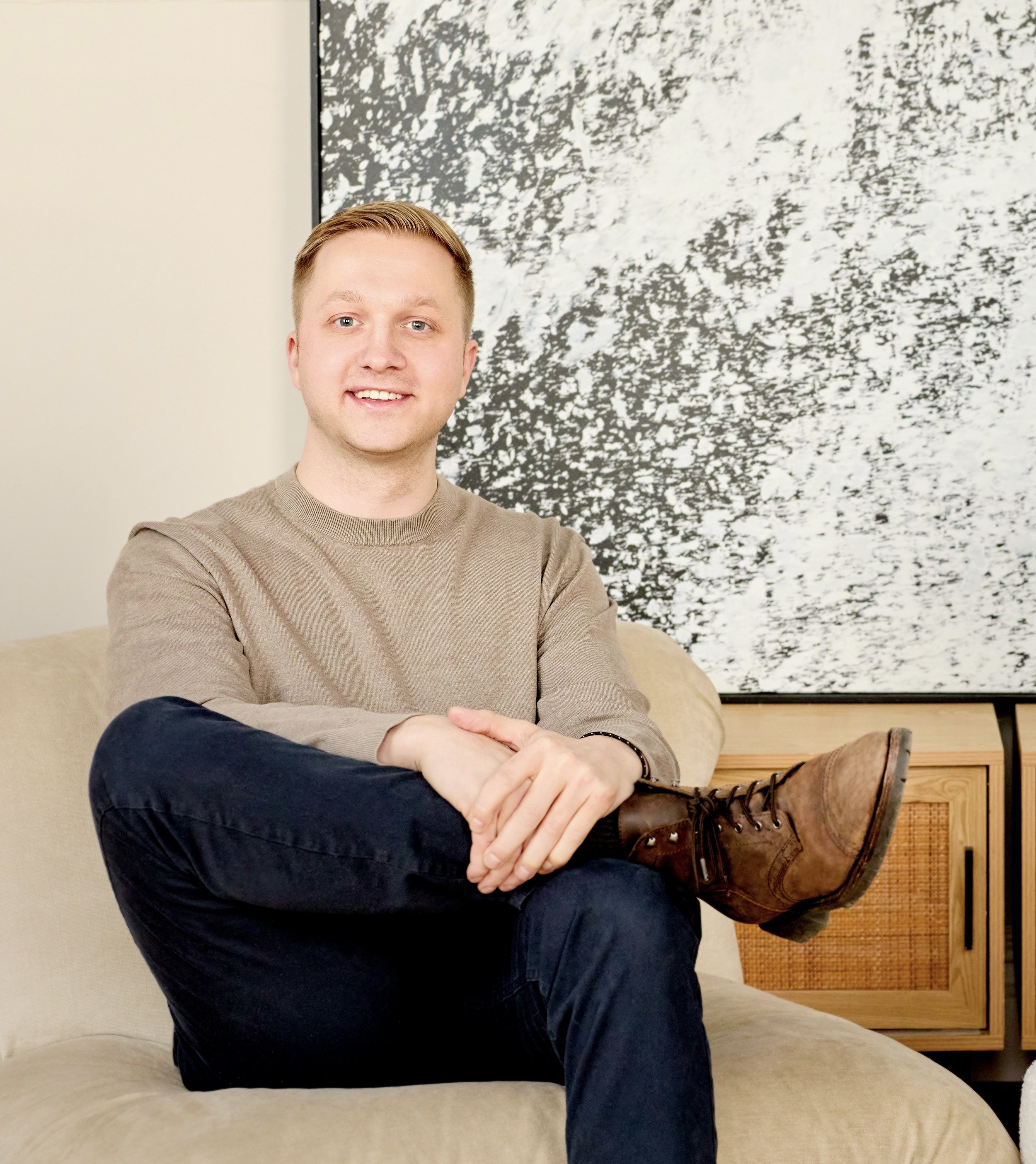 Jack Szary, LMHC-D, seated and smiling in front of abstract artwork