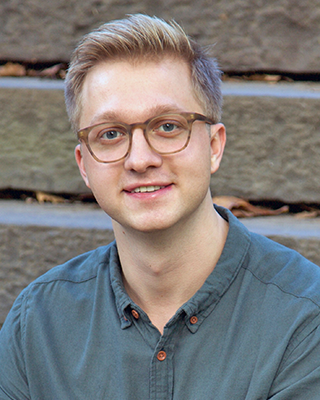 Jack Szary, LMHC-D, therapist at Rhythm Wellness, seated outdoors on stone steps