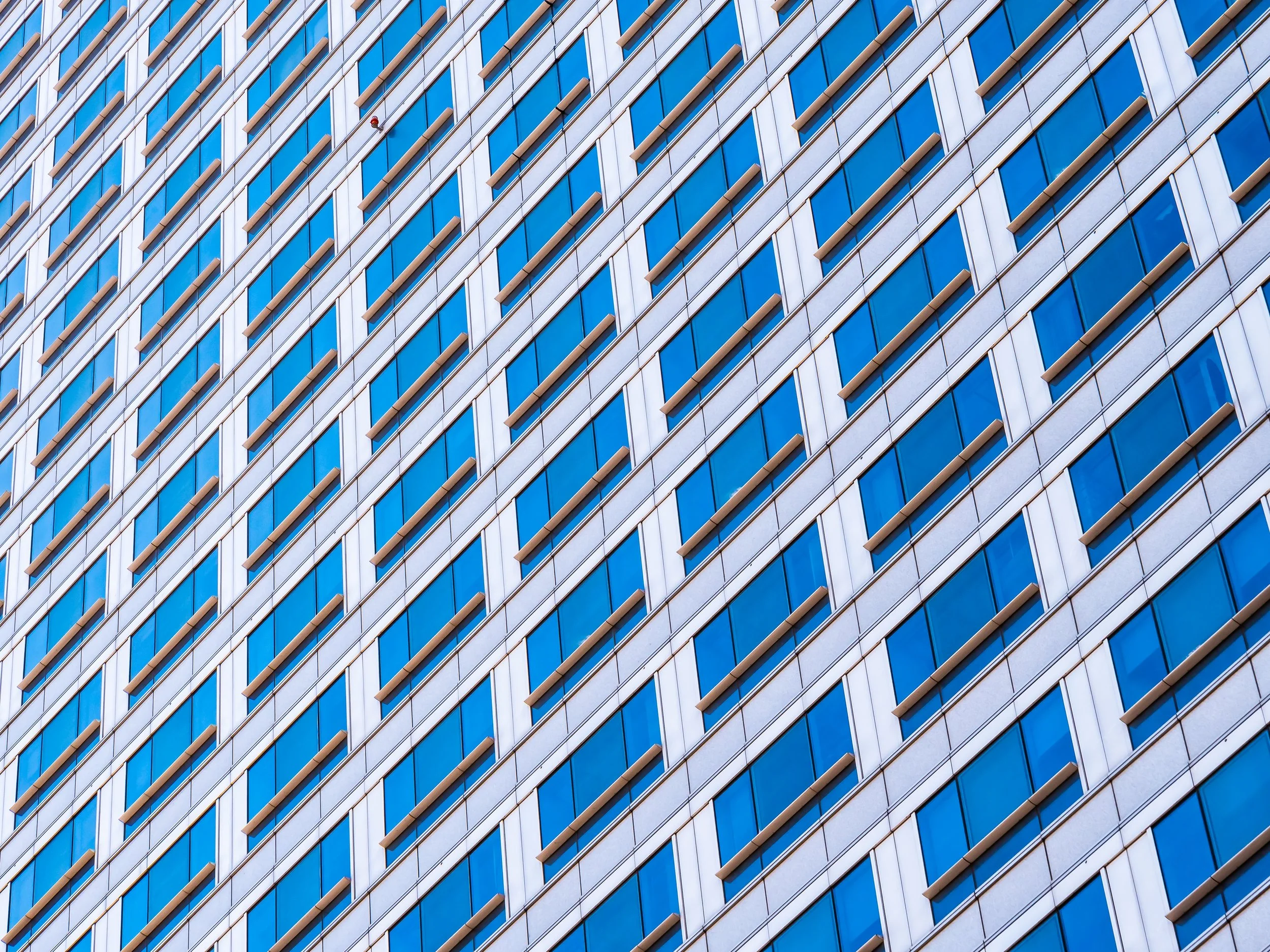 Close-up of a modern building's exterior with repeating diagonal blue glass windows and beige frames.
