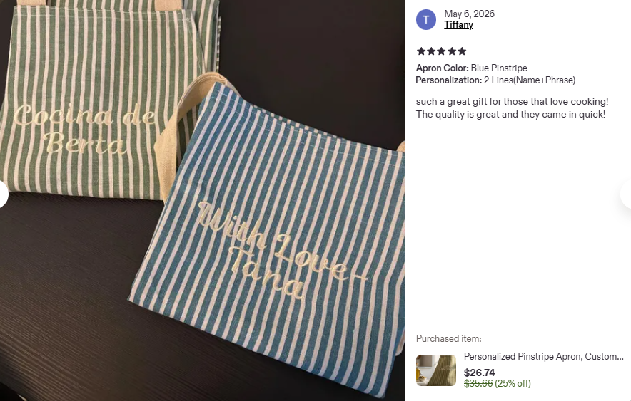 Two striped personalized aprons with embroidered text, one green and white and one blue and white, placed on a dark surface. The green apron reads 'Cocina de Berta' and the blue apron reads 'Wish I was Thin'.
