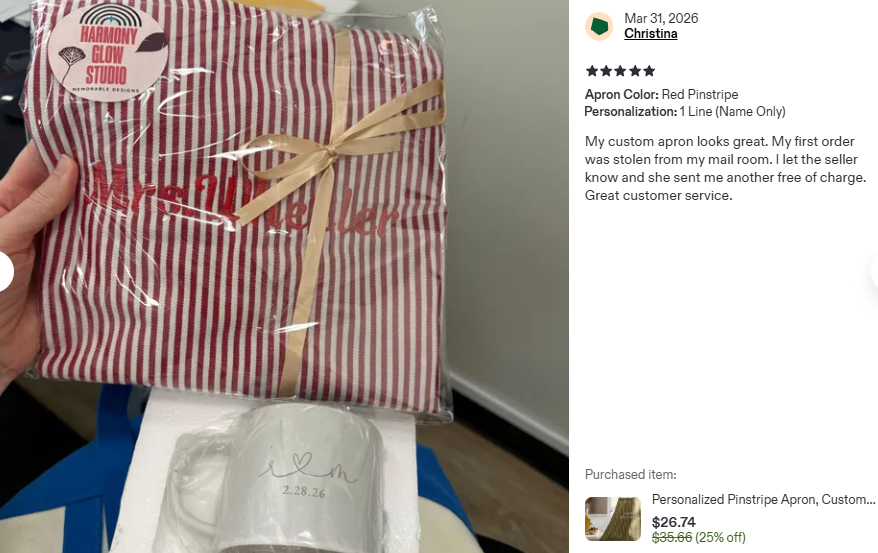 A red pinstripe apron packaged in clear plastic with a beige ribbon tied in a bow, and a white mug with a heart and the date 2.28.26 written on it.