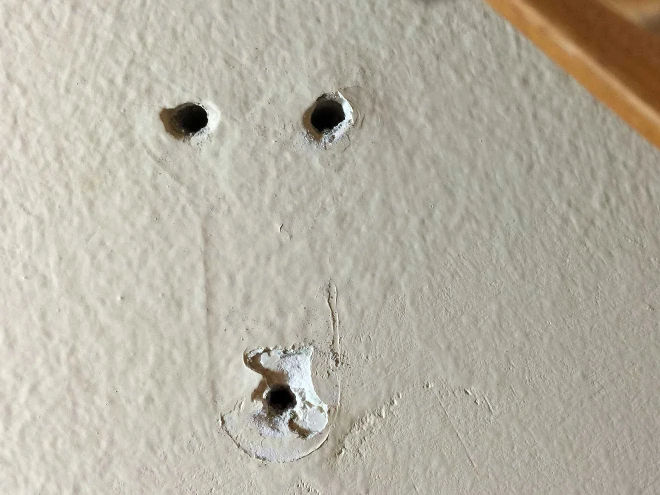 A close-up of a beige wall with three holes. About to be wall patched in NYC.