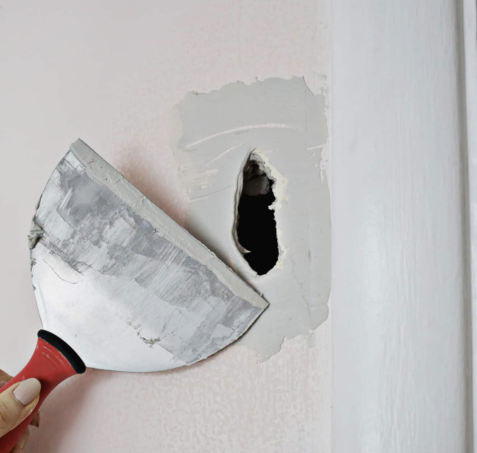 Someone using a putty knife to remove wallpaper from a wall.