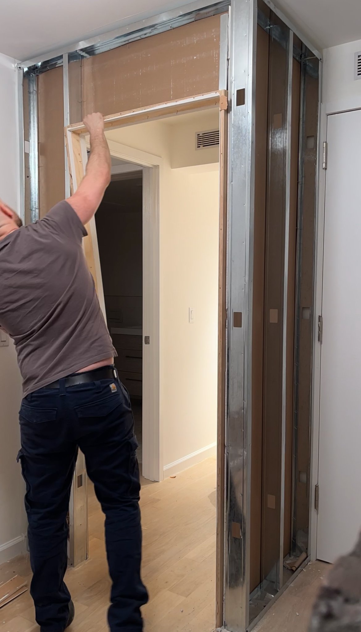 A person installing a new door frame in a partially built interior wall, with metal framing and drywall visible.