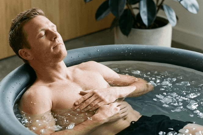 Man relaxing in a hot tub with water and bubbles, eyes closed, indoors near a potted plant.