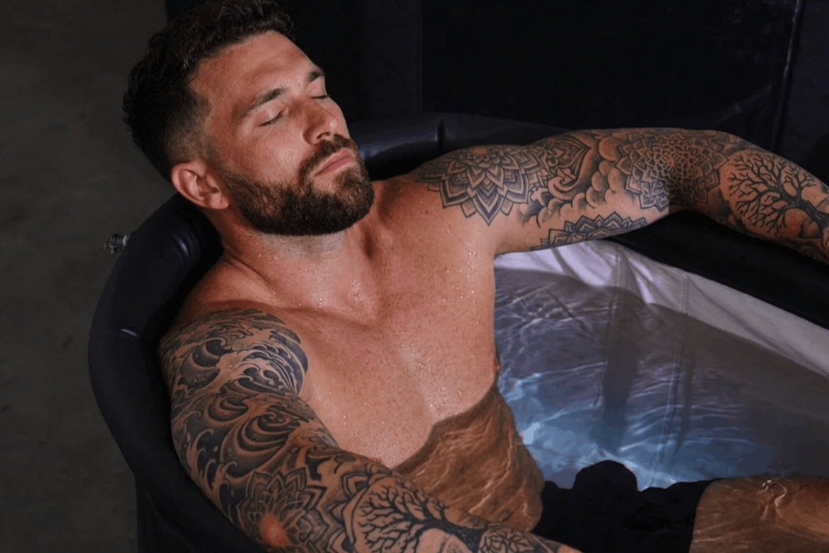 A man with tattoos relaxing in a pool with his eyes closed.