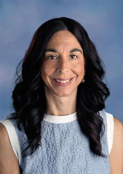 A woman with long dark hair smiling against a blue background.