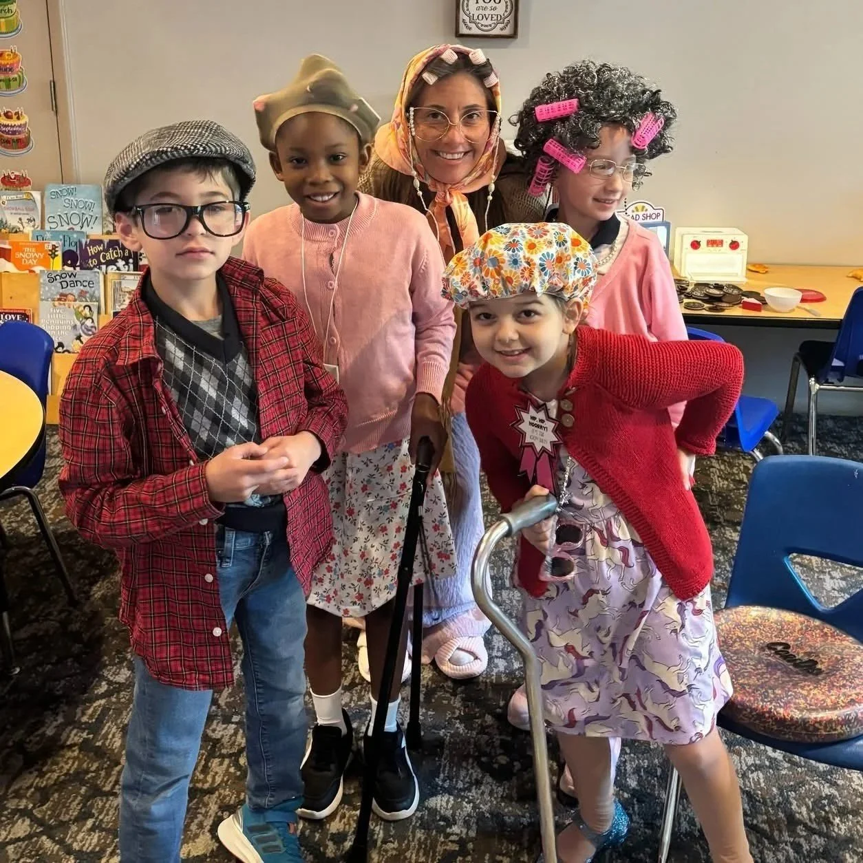 Group of children and adult dressed in themed costumes for a play or celebration, standing in a room with books and chairs.