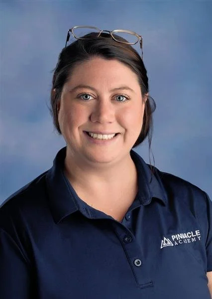 A young woman with long brown hair, glasses, and a white t-shirt smiling in front of a blue background.