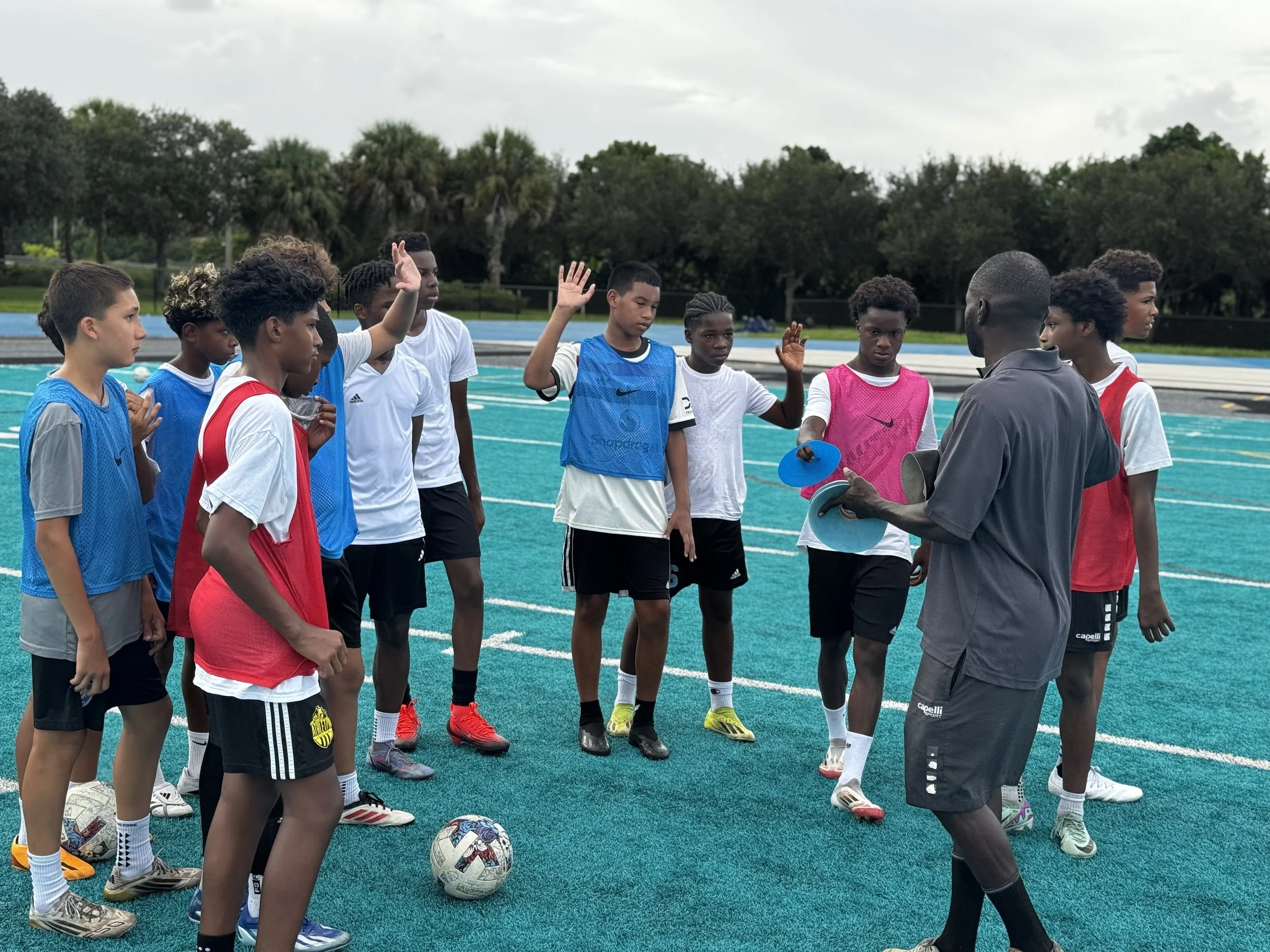 A group of young male soccer players listening to their coach during a practice on a turf field.