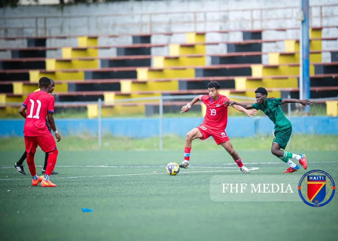 Three young soccer players practicing on a field, two in red jerseys and one in green, during daytime in Haiti.