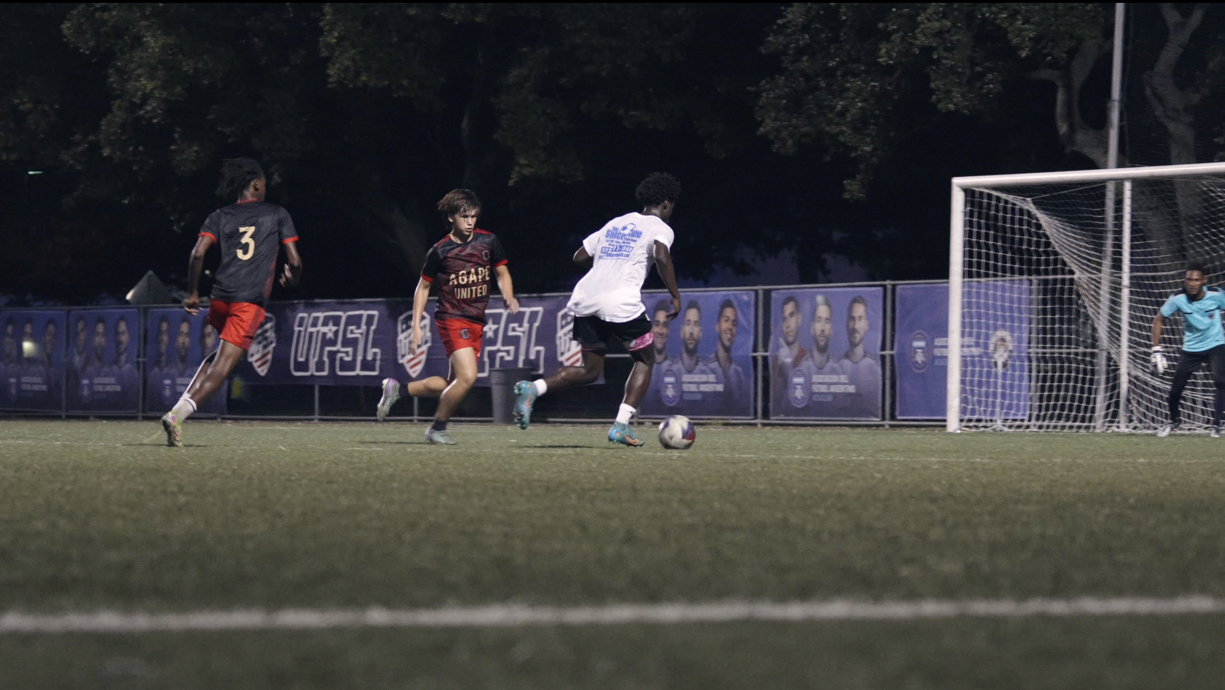 Soccer players competing for the ball on a field at night, with a goalie near the goal
