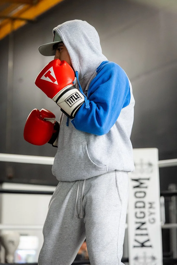 A person wearing a hoodie and sweatpants practicing boxing in a gym.