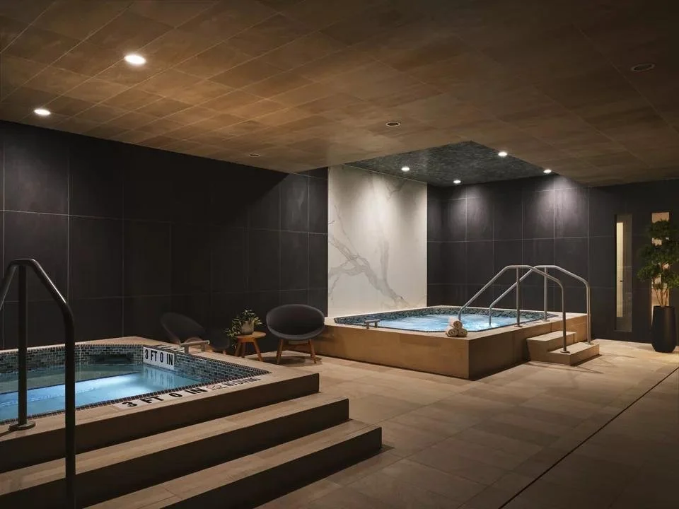 Indoor spa area with two hot tubs, comfortable chairs, plants, and dim lighting.