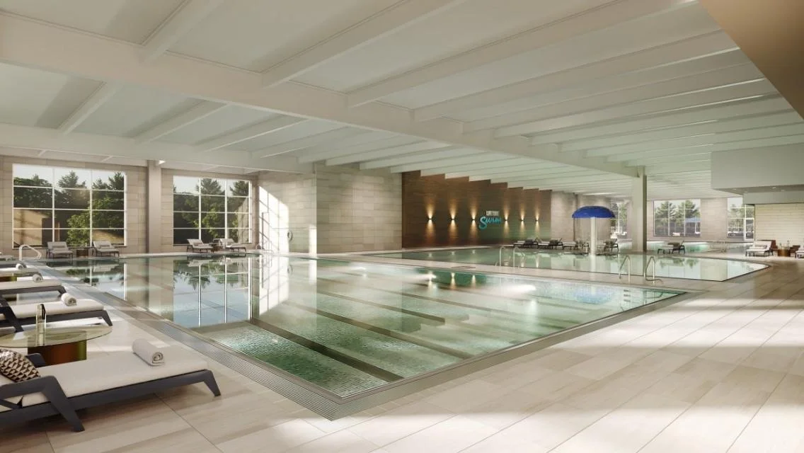 Indoor heated swimming pool area with lounge chairs, large windows, and a wooden accent wall with lighting.