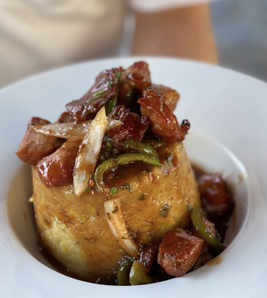 Cornbread topped with cooked sausage, green bell peppers, onions, and sauce, served in a white bowl.