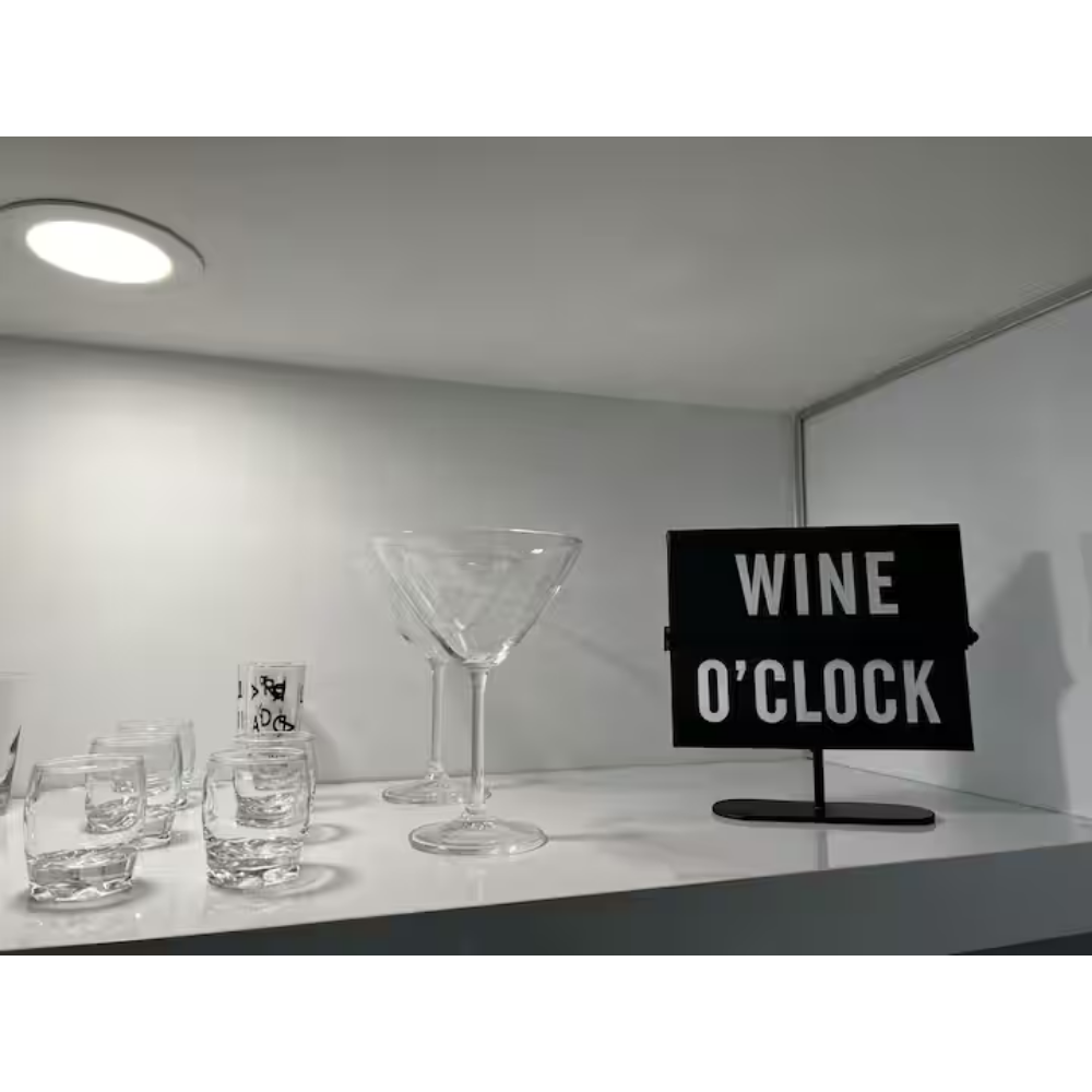 A display of glassware, including several shot glasses, an empty martini glass, and a large cocktail glass, with a sign that reads "WINE O'CLOCK" in the background.