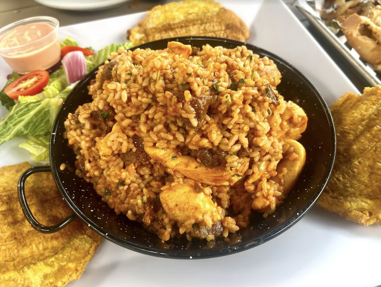 A plate with a serving of seasoned rice, garnished with vegetables, along with fried fish fillets, side salad, and dipping sauce.