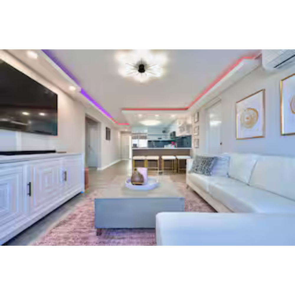 Modern living room with white sofa, wall art, and a TV, open to the kitchen with bar stools and decor.