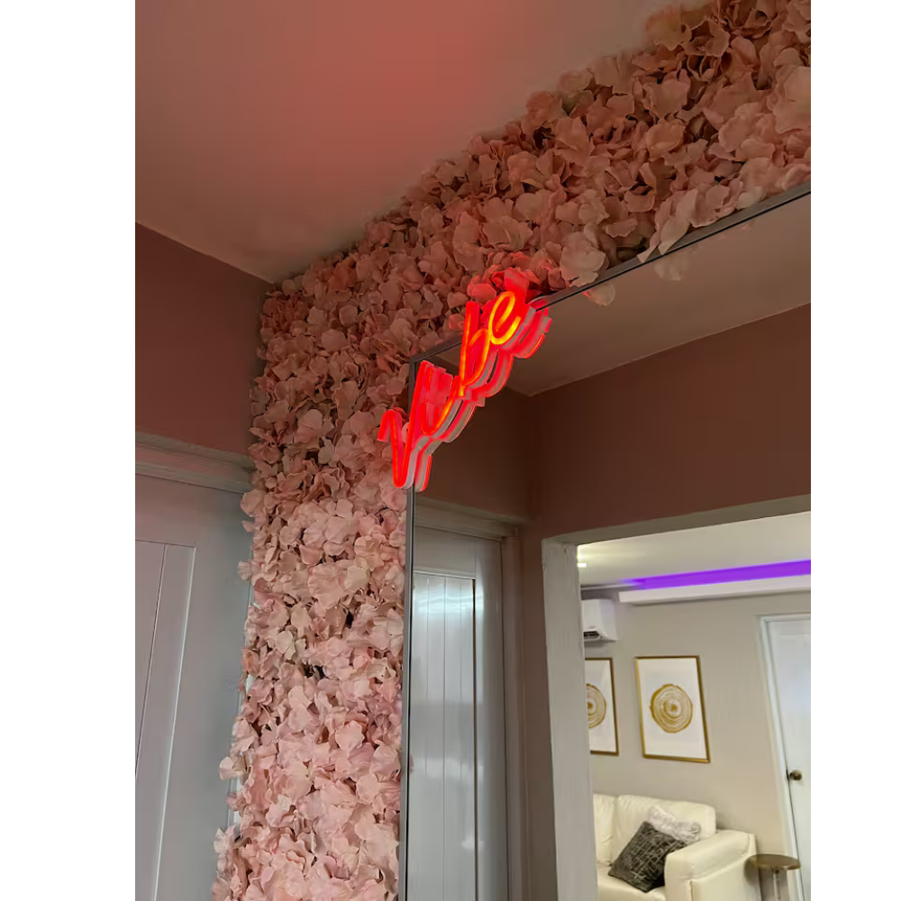 A doorway decorated with pink petals and a neon sign that says 'LOVE' in red and yellow, with part of a living room visible through the doorway.