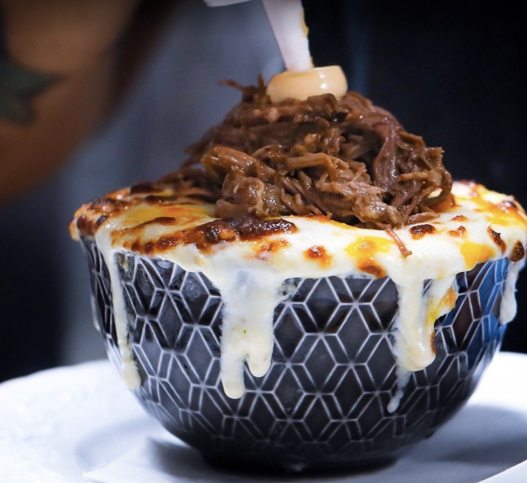 A bowl with melted cheese and shredded beef being topped with a dollop of sauce.