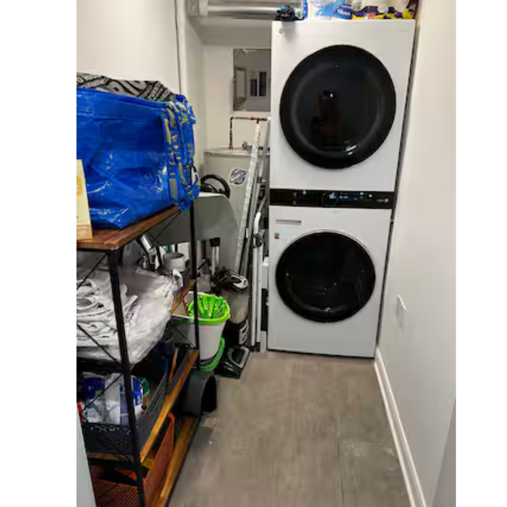Laundry room with stacked washer and dryer, shelves with cleaning supplies and bags, and various laundry tools and supplies.