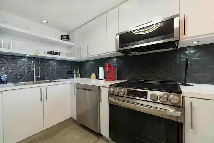 Modern kitchen with white cabinetry, black textured backsplash, stainless steel appliances including a dishwasher and oven, black-and-white countertops, and small kitchen accessories.