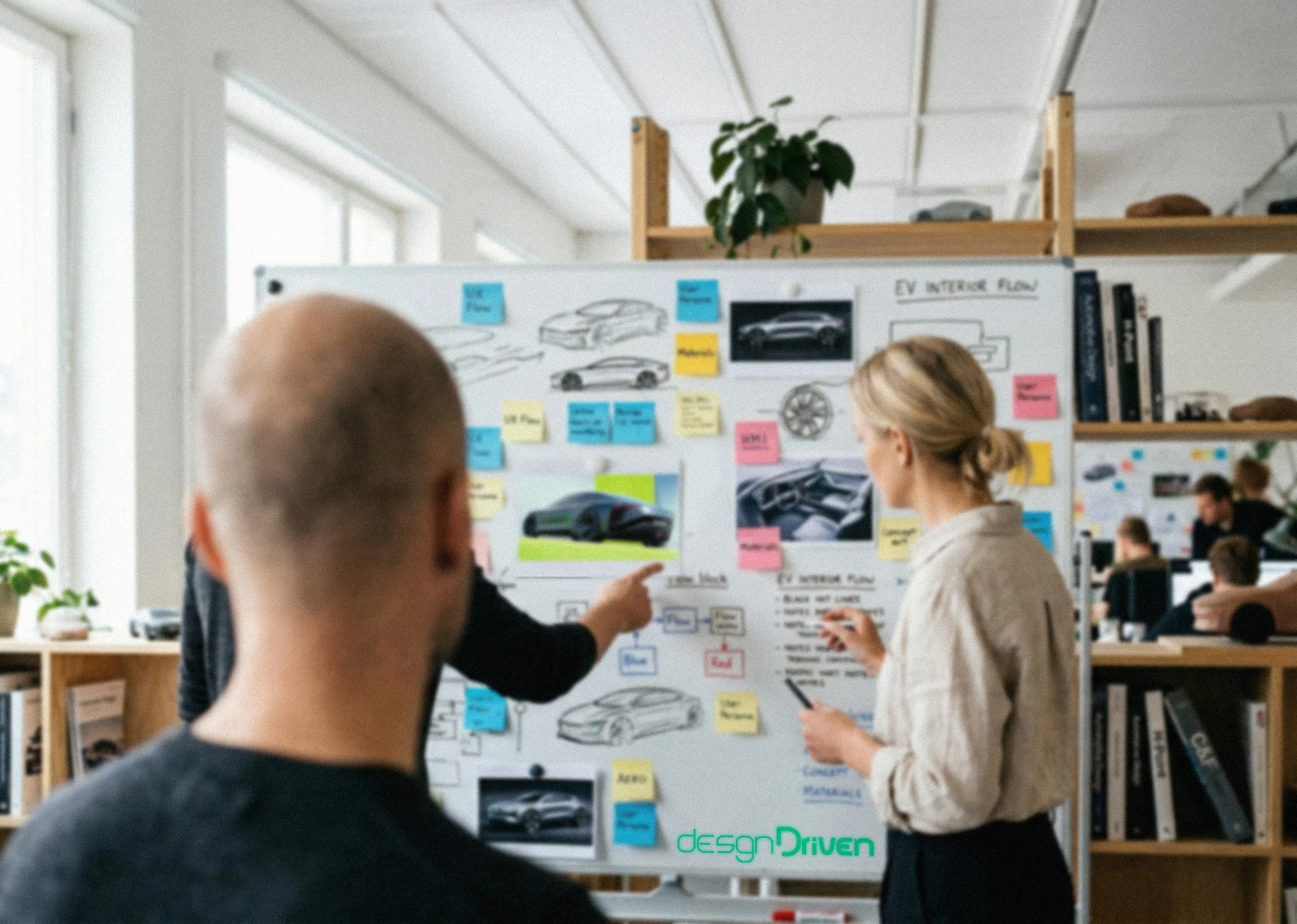 People discussing automotive design concepts on a whiteboard in an office or classroom setting.