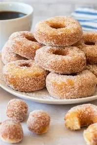 A plate of glazed mini donuts with a cup of coffee in the background.