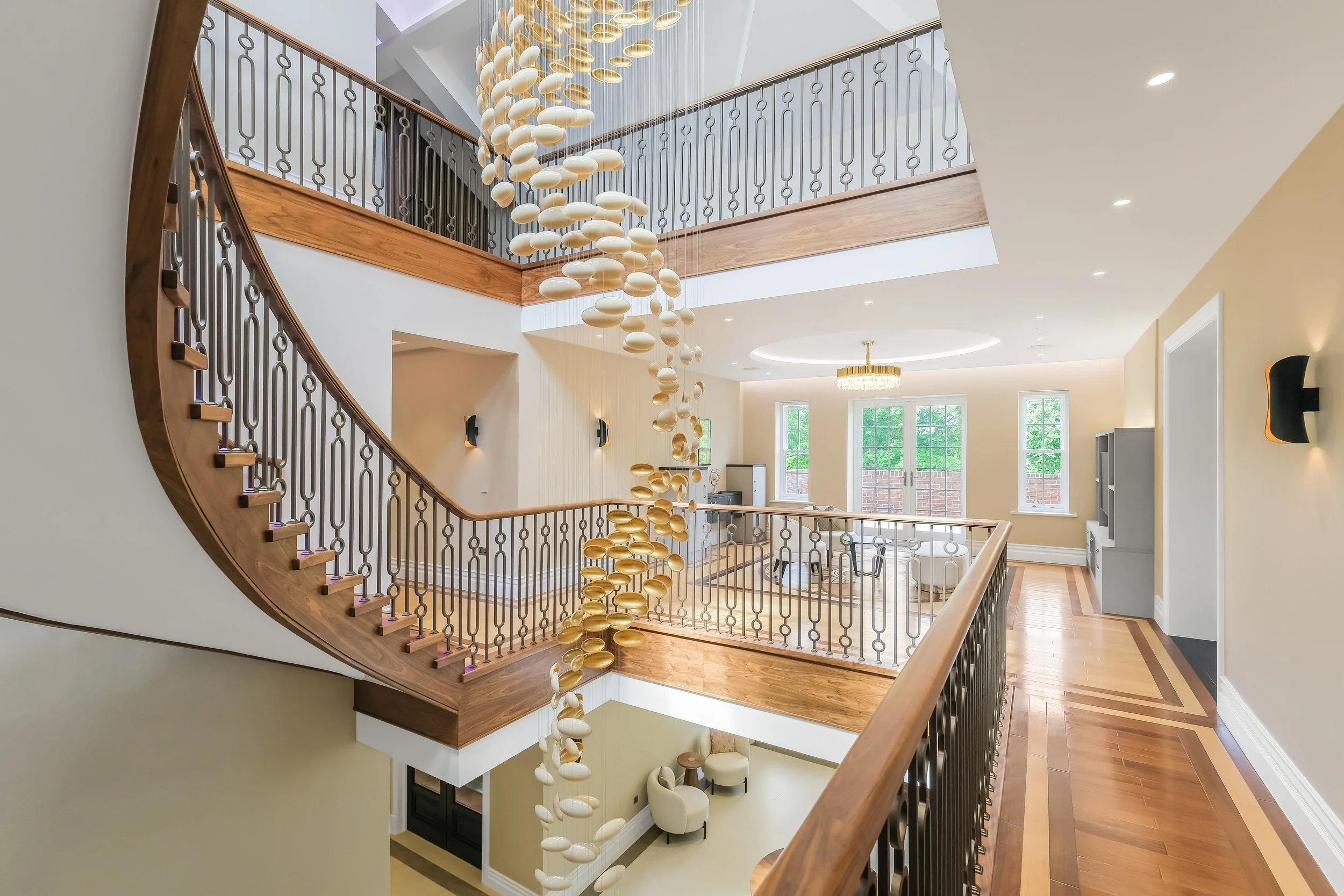 Interior view of a modern house with a wooden staircase, a glass chandelier hanging from the ceiling, and large windows letting in natural light.