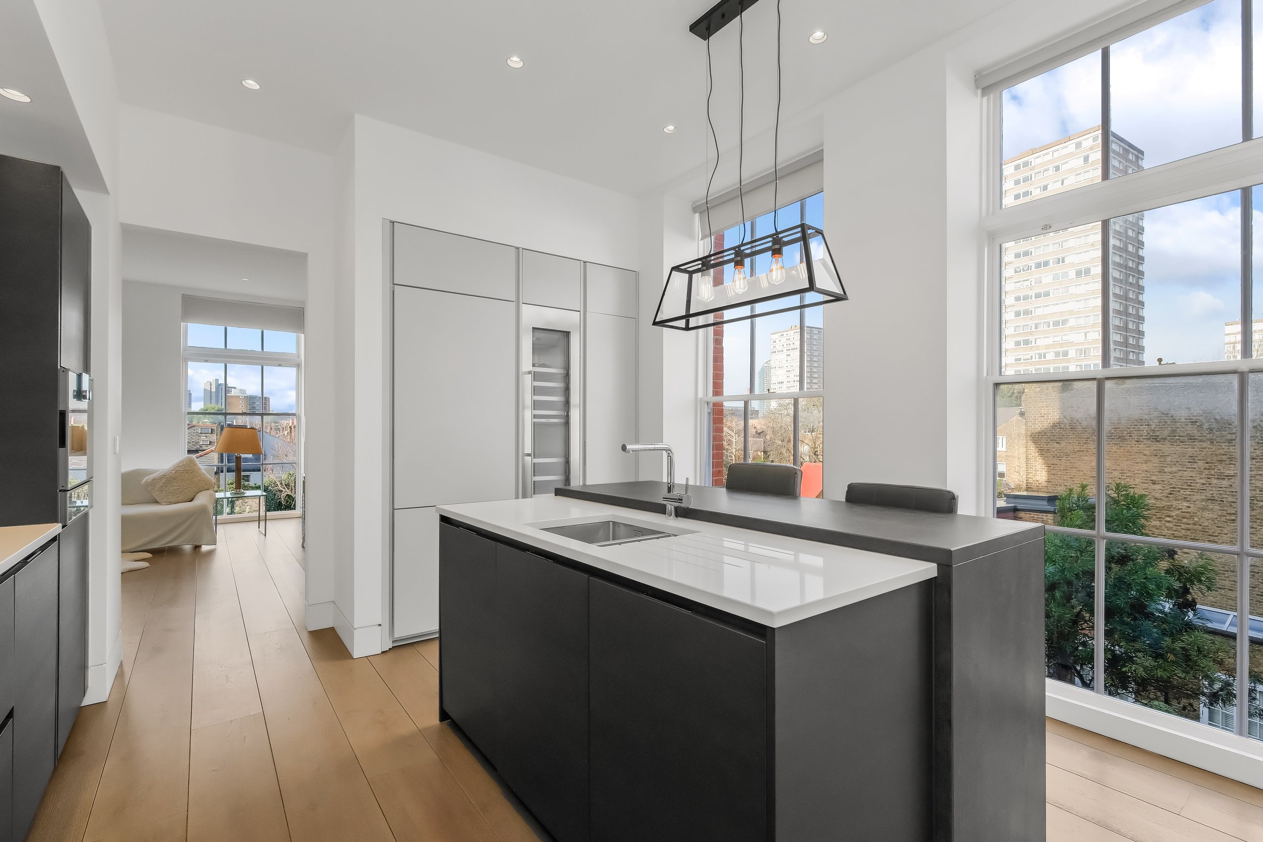 Modern kitchen with large windows, kitchen island with a sink, pendant lighting, and city skyline view.