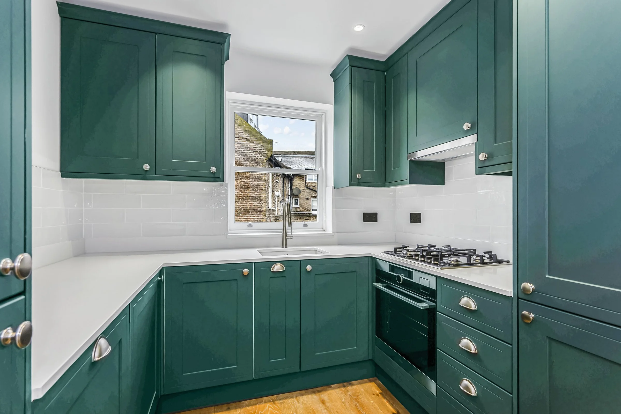 A kitchen with green cabinets, white countertops, a window showing buildings outside, and a gas stove.