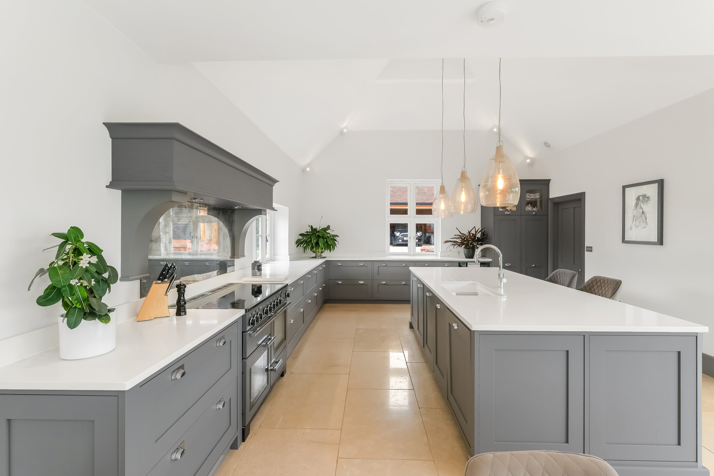 Modern kitchen with gray cabinets, white countertops, pendant lighting, and plants.