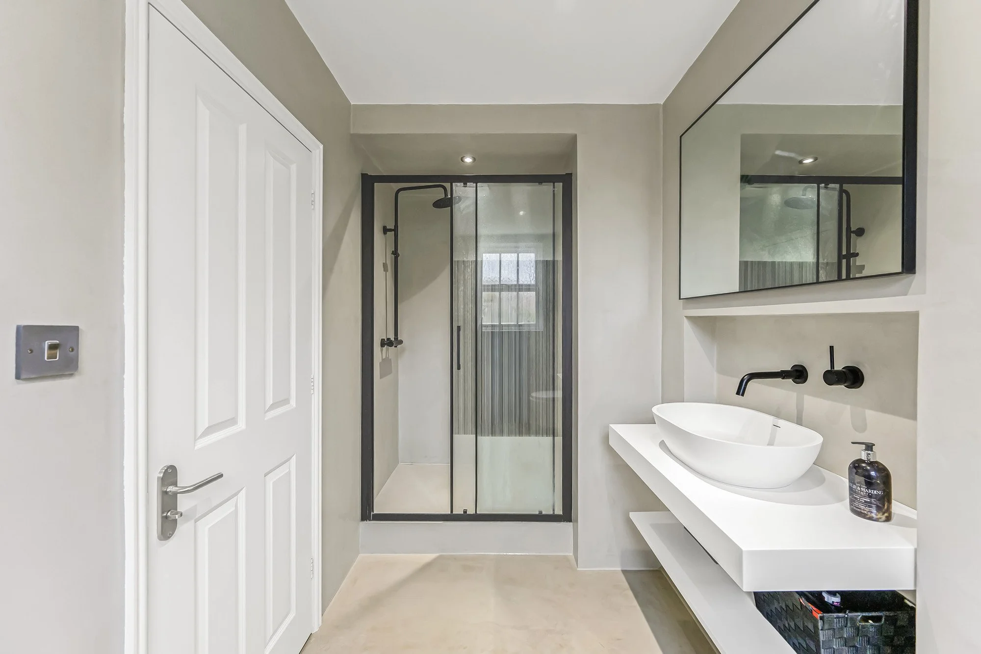 A modern bathroom with a walk-in shower, white sink with black fixtures, and a large mirror.