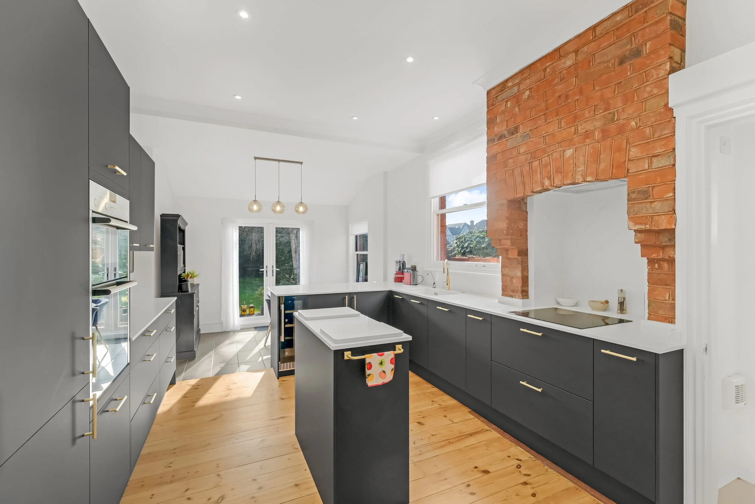 Modern kitchen with black cabinets, white countertops, a brick chimney, and large windows letting in natural light.